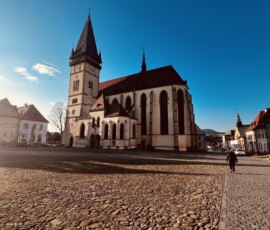 Historický kostol s vysokou vežou na námestí, zachytený za jasného dňa.