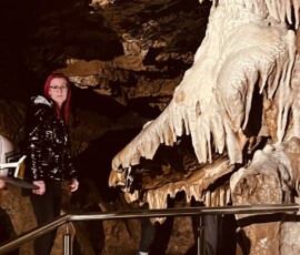 Turisti v jaskyni s výzdobou stalaktitov a stalagmitov.
