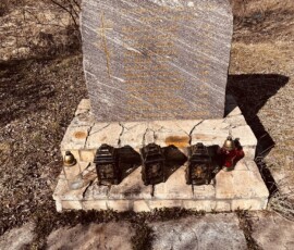 Pamätník na ceste s krížom a sviečkami, umiestnený na kamennom podstavci v prírodnom prostredí. Pamätník na ceste s krížom a sviečkami.