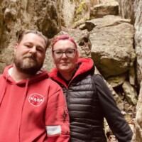 Dvaja ľudia na výlete v prírode, oblečení v teplých bundách, v skalnatom prostredí počas výletu. Dvaja turisti v prírode medzi skalami, oblečení v teplých bundách.