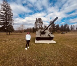 Historické delo na otvorenom priestranstve s osobou v popredí, modrou oblohou a stromami.