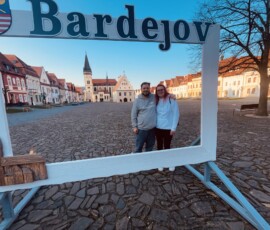 Fotografia dvoch ľudí stojacich v historickom centre Bardejova s názvom mesta v popredí.