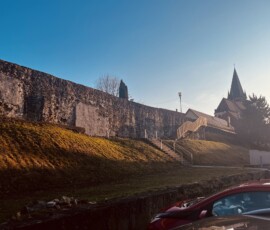 Historické mesto s kostolom a hradbami na cestách, zachytené počas dňa s modrou oblohou.