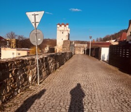 Veža na ceste v Šuhajovciach s modrou oblohou a kamenným chodníkom.