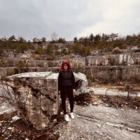 Obrázok s členkou skupiny Šuhajovci počas výletu v prírode, obklopený skalami a prírodou. Členka skupiny Šuhajovci na výlete v prírodnom prostredí s skalami a stromami.