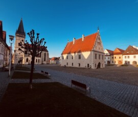 Námestie v Suhájo-vciach s historickými budovami a kostolom na pozadí.