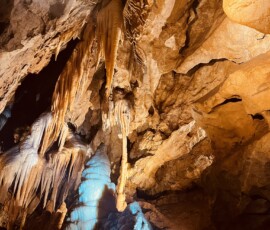 Vnútro jaskyne s stalaktitmi a stalagmitmi, osvetlené farebným svetlom.