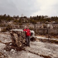 Fotografia zachytáva muža v červenom tričku stojaceho pri veľkom kameni v skalnatom teréne, súčasť výletu po Slovensku. Turista stojaci pri veľkom kameni v prírodnom prostredí, objavovanie krásy Slovenska, outdoorové akt.