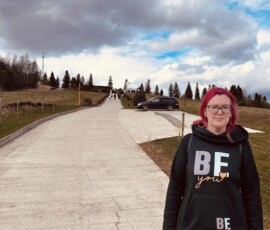 Žena na ceste počas výletu Šuhajovci na cestách, príroda a obloha v pozadí.