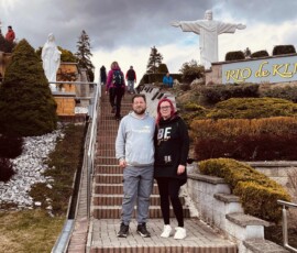 Skupina turistov na výlete pri sochách Krista v Riu de Janeiro, s dramatickou oblohou na pozadí.